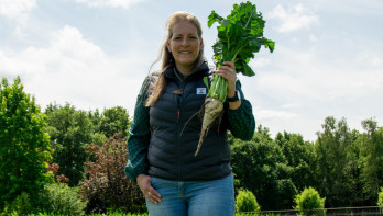 Een vrouw staat lachend in een veld met een suikerbiet in haar hand