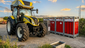Gele tractor die waterstof tankt bij een installatie met rode gascilinders op een boerenerf.