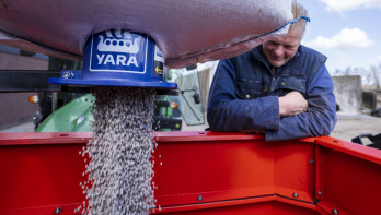 Boer vult een kunstmeststrooier terwijl korrels uit een Yara-bigbag naar beneden stromen.