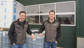Twee mannen staan voor een landbouwloods naast containers met agrarische producten