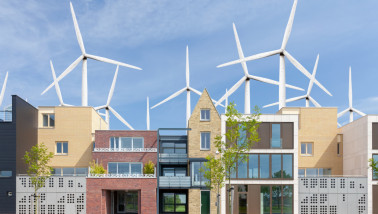 Rij moderne Nederlandse gezinswoningen met op de achtergrond een veld met grote windturbines.