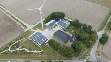 Luchtbeeld met drone van een modern landbouwbedrijf met zonnepanelen en een windturbine.