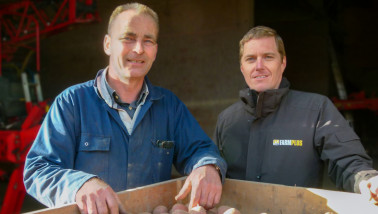 Twee mannen poseren bij een kist aardappelen