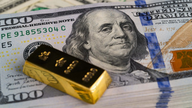 Close-up of a gold bar lying on a stack of new US $100 bills