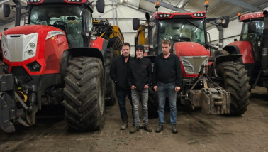 Drie mannen staan voor een rij rode trekkers