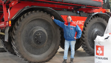Een man poseert lachend bij een zelfrijdende veldspuit.