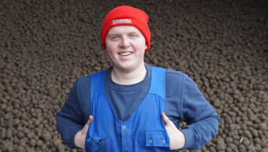 Een man staat lachend voor een stapel aardappelen