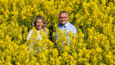 Twee personen staan lachend in een veld met koolzaad