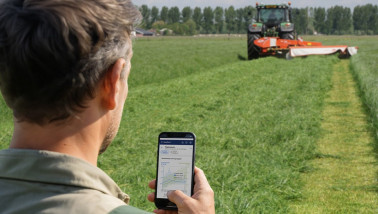 Boerderijwerker volgt de grasoogst via een app terwijl een tractor het veld maait.