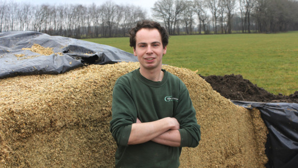 Een man staat met zijn armen over elkaar voor een berg met gehakselde mais