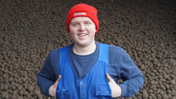 Een man staat lachend voor een stapel aardappelen