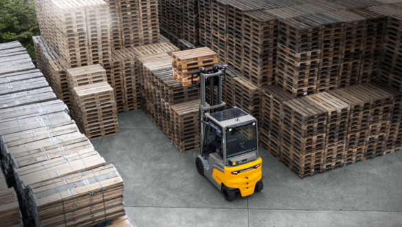Elektrische Jungheinrich-heftruck rijdt tussen grote stapels houten pallets op een opslagterrein.