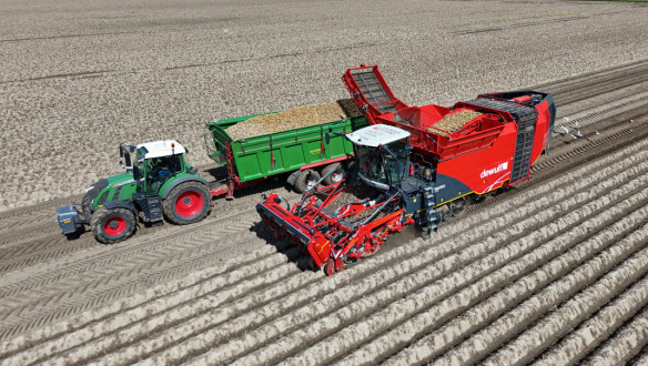 Aardappelrooier oogst aardappelen naast een tractor met volle kiepwagen.