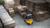 Elektrische Jungheinrich-heftruck rijdt tussen grote stapels houten pallets op een opslagterrein.