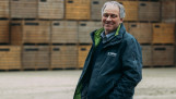 Guus Bergmans poseert lachend voor stapels met kratten